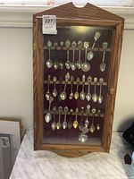 Overall view of wooden display cabinet with 38 souvenir spoons mounted inside against red felt
