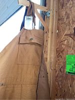 Front view of brown insulated canvas coveralls hanging, showing shoulder strap and chest pocket.