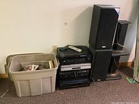 Full view of stacked electronics, speakers, and bin of media discs on carpeted floor.