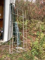 Aluminum garden frame leaning against a structure outside, showing its size and condition with fencing posts and plastic fence behind