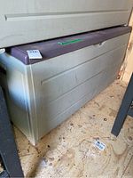 Side and front view of the Keter resin garden box showing gray plastic body with textured horizontal panels and dark lid.