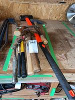 Lot of various hammers with wooden and fiberglass handles, pick axe and sledgehammer on a wooden workbench.