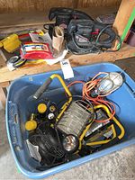 Photo of blue plastic tote containing construction lights, flashlights, cords, and other lighting equipment along with sandpaper.