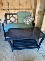 Coffee table with glass top and love seat with cushions and one patterned pillow. Shows some wear and stains on cushions.