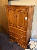 Photo of solid pine highboy dresser showing two cupboard doors above and three drawers below with round knobs, visible light scuffs on surface.