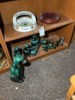 Overview photo showing 2 porcelain ashtrays on upper shelf and multiple green pottery animal figurines on middle shelf and floor
