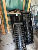 Overview of four black resin loading ramps leaning against wooden shelves and three steel trailer hitches placed on top