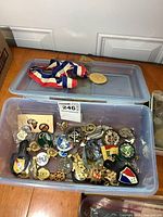 Plastic bin filled with various vintage service badges and pins with visible medals and cloth ribbons.