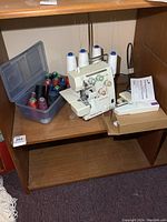 Singer differential feed sewing machine with thread spools and manual on wooden shelf.