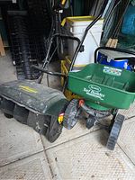 View of Yardworks electric snow thrower next to Scotts Turf Builder mini seeder with yellow milk crate and pails behind.