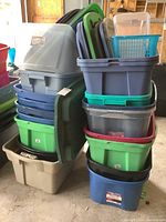 Side view of stacked various sized plastic tote bins and lids in multiple colors including green, blue, and grey.