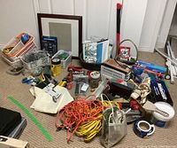 Overall lot of assorted utility supplies including extension cords, hand tools, hardware, and home improvement items on carpeted floor.