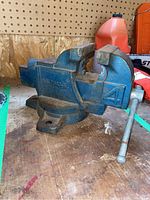 Blue metal bench vise on wooden workbench, showing side view with model number 58-7843-6 and number 4 cast in metal.
