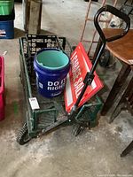Photo of green metal wagon with mesh sides, wheels, handle, blue bucket, and garage sale signs inside.