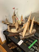 Photo showing the 3 wooden sailing ship models placed on a black plastic table surface. Each model has multiple beige sails and rigging details.