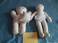 Front view of two voodoo dolls side by side on blue cloth background with yellow note.