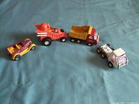 Four vintage toy vehicles including a funny car, cement mixer truck, dump truck, and white truck on blue surface.