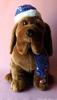 Front view of a brown plush dog with a blue sequined Santa hat and matching scarf showing facial features and front paws.
