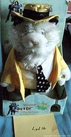 Front view of plush white animated cat toy in original branded packaging showing yellow jacket, polka dot tie and hat.