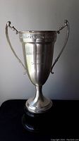 Front view of the large silver-colored trophy showing the full height and handles on a black base.