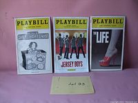 Photo shows three vintage Playbills standing upright, featuring covers for The Allergists Wife, Jersey Boys, and The Life, with a handwritten label 'Lot 33' in front.