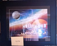 Framed colorful Hollywood sign print with a surreal space background including a planet or moon and bright light effects. Print size about 25 inches wide by 21 inches tall.