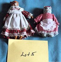 Two porcelain bear dolls shown front view wearing distinct vintage dresses and aprons with lace detailing.