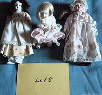 Photo showing 3 porcelain dolls laid out on fabric background with a card labelled Lot 8 in front.