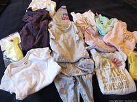 Various girls baby clothes laid out showing designs, colors, and types of garments