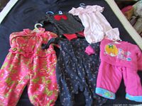 Five pieces of child's clothing arranged on a bed, showing floral patterns, solid colors, and appliques.