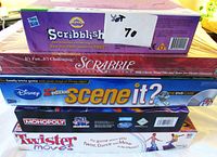 Stack of boxed games including Scribblish, Scrabble, Scene It? 2nd Edition Disney DVD game, Monopoly Space Edition, and Twister Moves
