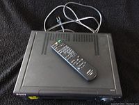 Sony DVD player with ventilation slots and Sony remote control on top placed on a black fabric surface.