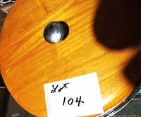 Top view of polished wood round lid of the ice bucket with metal knob handle and a label showing lot number 104.