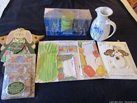 Photo shows a collection of new items including an Irish coffee glass set with candle, a white ceramic floral pitcher, vegetable-themed stationery, a spring-themed bunny decor, green plastic forks, and assorted paper goods.