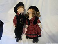 Boy and girl kissing porcelain dolls standing next to each other dressed in coordinated red and black outfits.