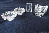 Four clear crystal and glass items on dark fabric: two candle sticks, one candy dish, one paperweight with bird etching.