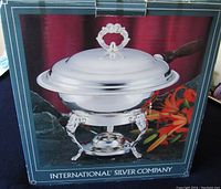 Photo of the sterling silver warmer in original box showing polished silver warmer with ornate lid handle and wooden handle, on a stand with decorative legs and burner