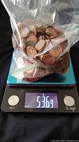 A plastic bag full of unsorted American pennies placed on a digital scale showing a weight of 5.36 pounds.