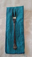 Full view of 6 inch sterling silver pickle fork resting on blue cloth bag