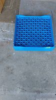 Blue plastic bread trays stacked on a concrete floor, showing lattice bases and metal side rails.