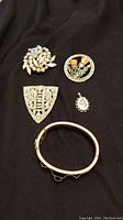 Costume jewelry lot on black fabric showing multiple pieces including brooches and bangles