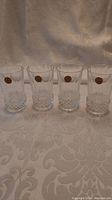 Four Cristal d'Arques juice glasses arranged in a row on a fabric surface, showing overall appearance and condition.