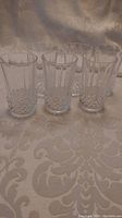 Six clear Cristal d'Arques juice glasses arranged on a patterned tablecloth, showing full set from the front.