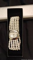 Photo of a new fashion watch with a rectangular mother of pearl style face and a multi-strand faux pearl bracelet band inside a black box.