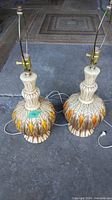 Pair of vintage ceramic side lamps, tall with decorative leaf motif, electrical cords shown.