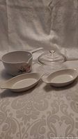 Photo of the full set showing the Corning France saucier with floral design and handle, Pyrex casserole, glass lid, and two Au Gratin dishes on a patterned fabric background.