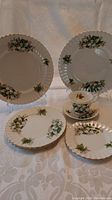 Various views of Royal Albert Trillium pattern china set including dinner plates, salad plates, dessert plate, cup and saucer with floral decoration and gold trim.