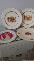 Four commemorative china plates with royal emblems and portraits arranged on a glass surface