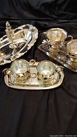 Photo showing assortment of silver plated trays, creamers, and sugar bowls on a black cloth background.