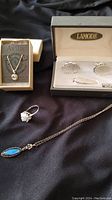 Photo showing assorted silver jewelry items on a black surface, including necklaces, rings, and earrings in a Lamode box.